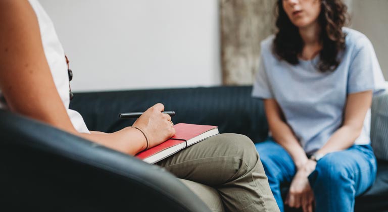 counselor with notebook in lap talking to patient sitting on sofa