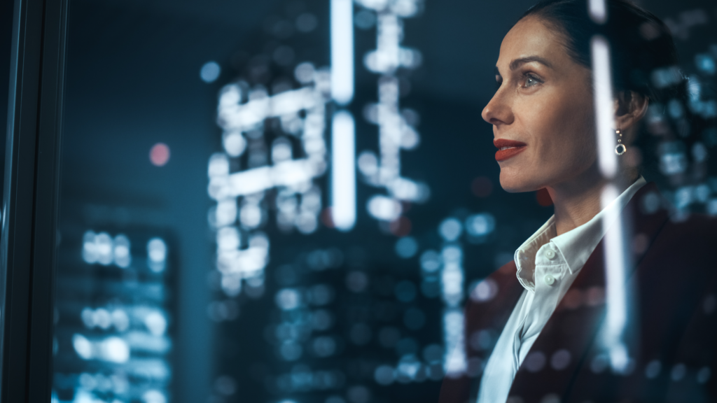 Professional businesswoman in white shirt gazing thoughtfully through office window at blurred city skyline at night