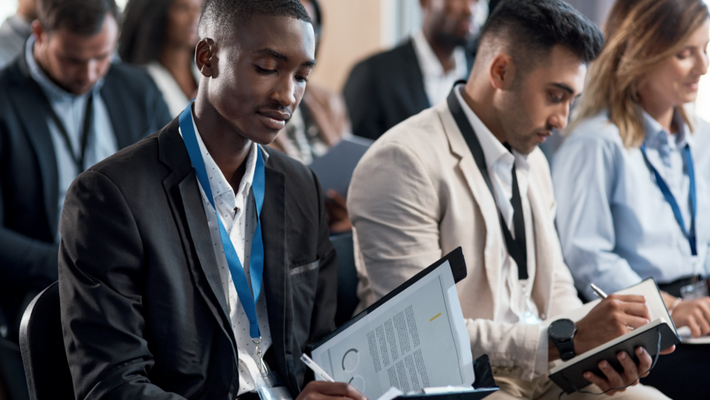 Diverse business professionals in suits with lanyards reviewing documents and taking notes at a professional conference